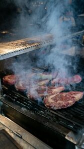 Close-up of juicy, seasoned steaks sizzling over a smoky grill, perfect for barbecue lovers.