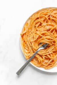 Close-up of a savory plate of spaghetti in tomato sauce on a white background.