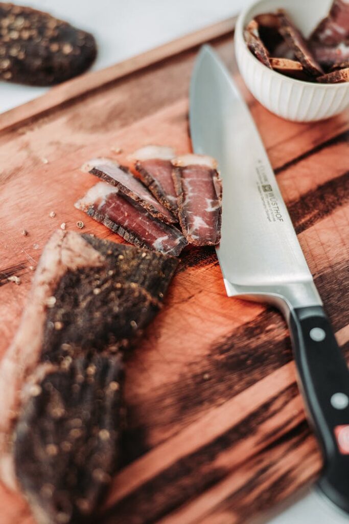 Cured meat slices on a wooden board with a chef's knife, perfect for food photography.